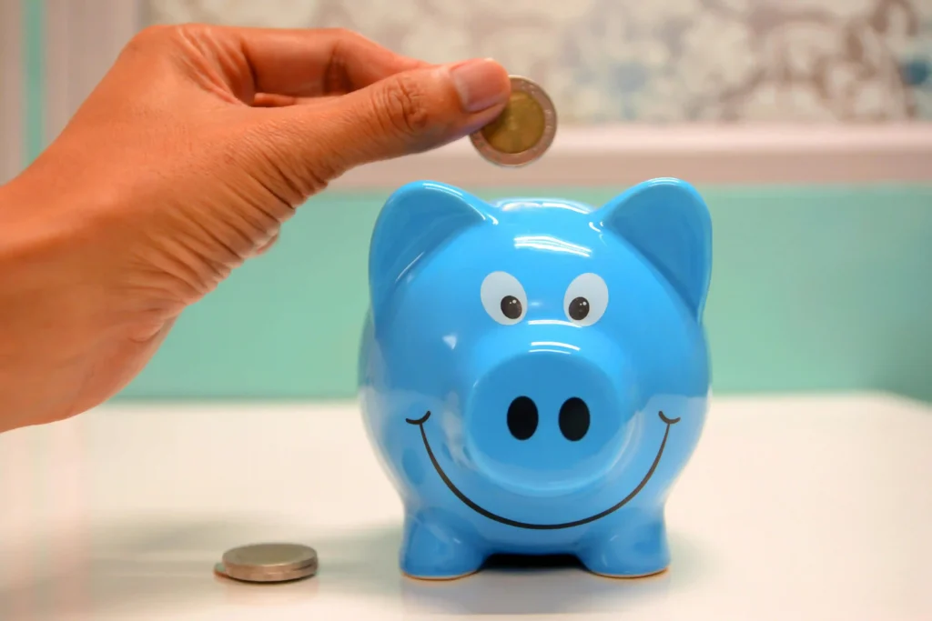 Hand placing a coin into a blue smiling piggy bank — symbolizing skincare savings and smart self-care investment. "Purellelife" watermark in corner.
