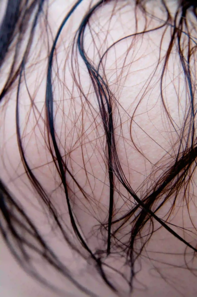 Illustration showing low porosity hair with tightly packed cuticles, represented by hair strands with a visual overlay. The image also highlights hair products sitting on the surface, water droplets not absorbing into the strands, and dry, coated roots. A clarifying shampoo bottle is shown to suggest cleansing to remove product buildup.